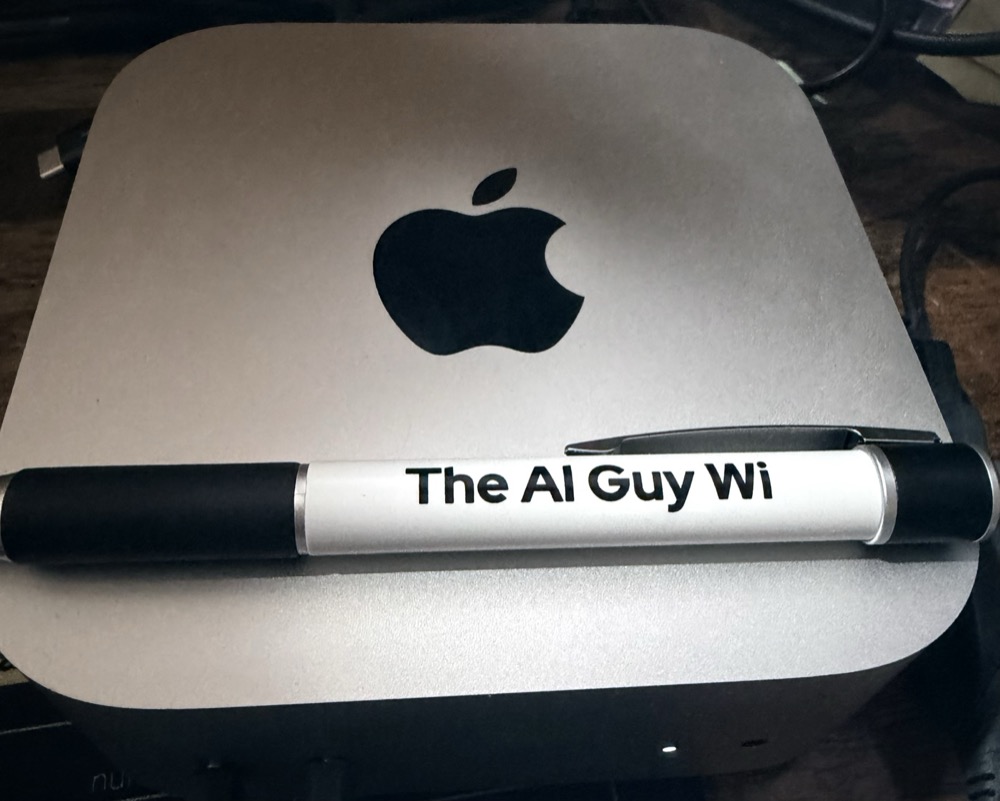 A Mac mini with a custom-branded 'The AI Guy WI' pen on top — the hardware Alex installs in client offices to host their Agent Logic stack